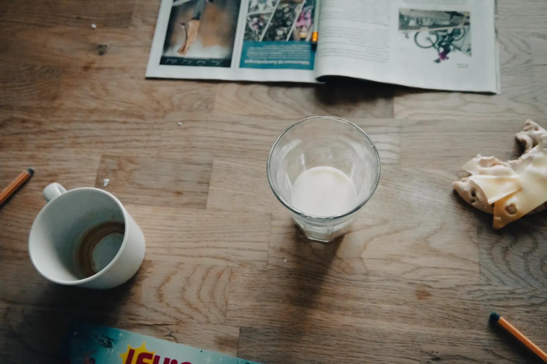 En kaffekopp, ett glas mjölk och en uppslagen tidning på ett träbord.