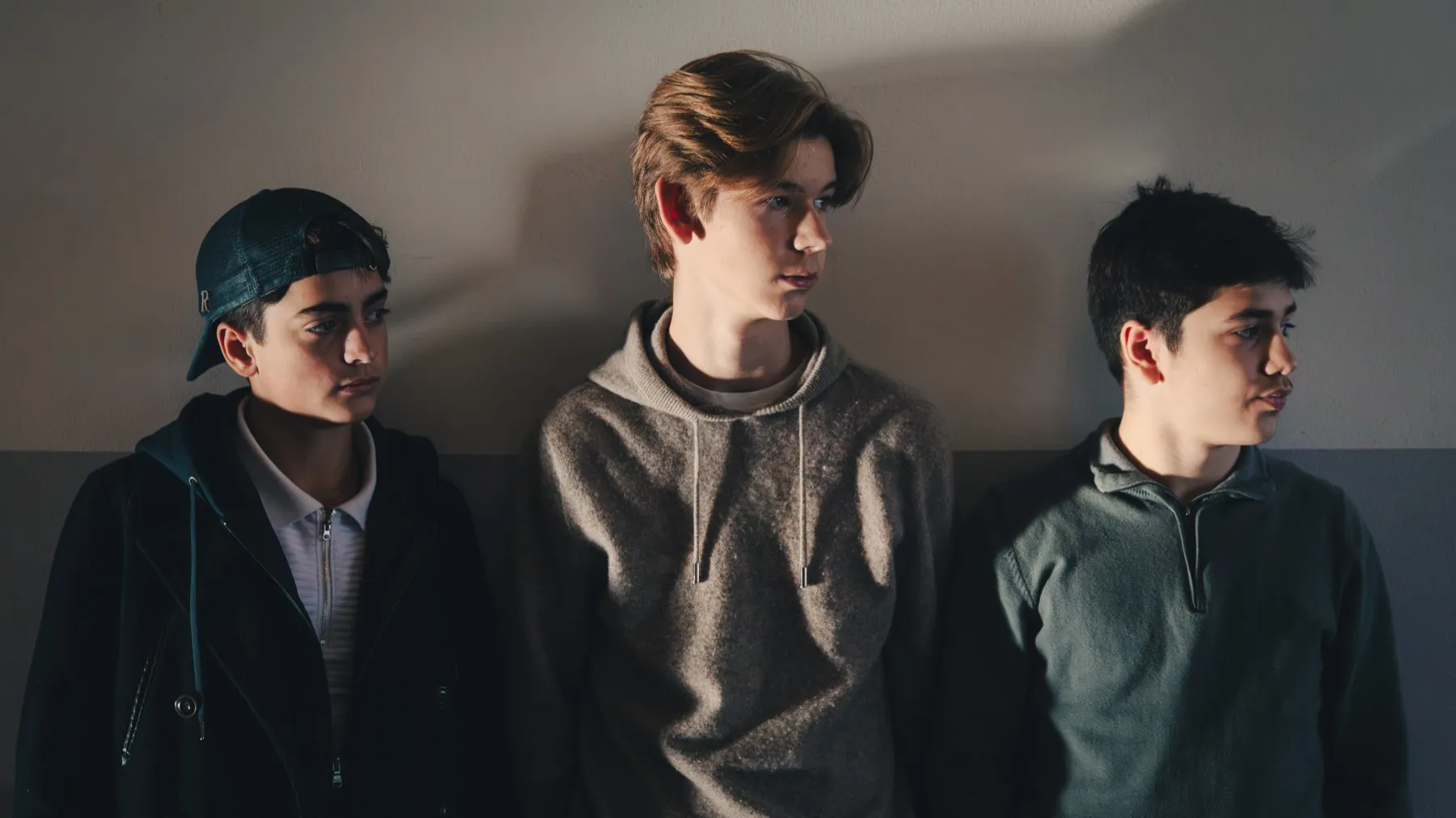 Three teenage boys standing against a wall.
